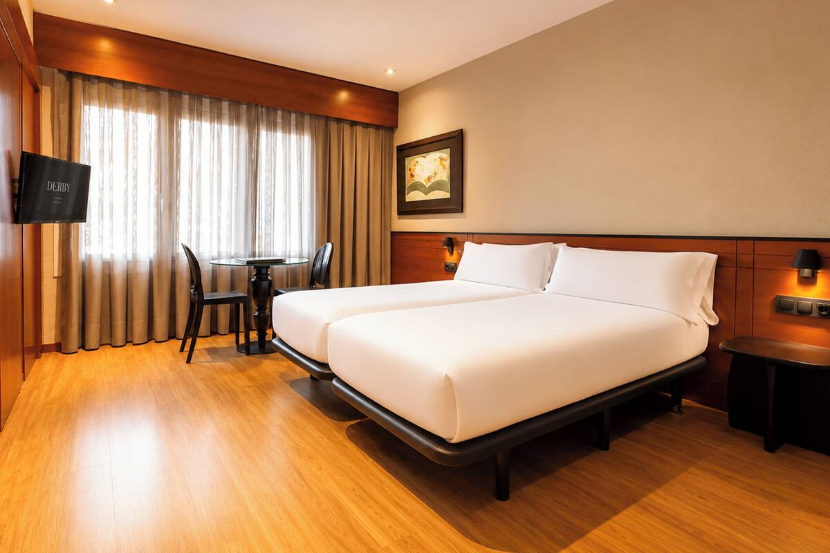 A hotel room with a bed, a desk, a chair, a television, and a painting on the wall.