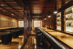 Uma área de bar com um balcão comprido, assentos em couro preto e uma parede de garrafas de vinho.
