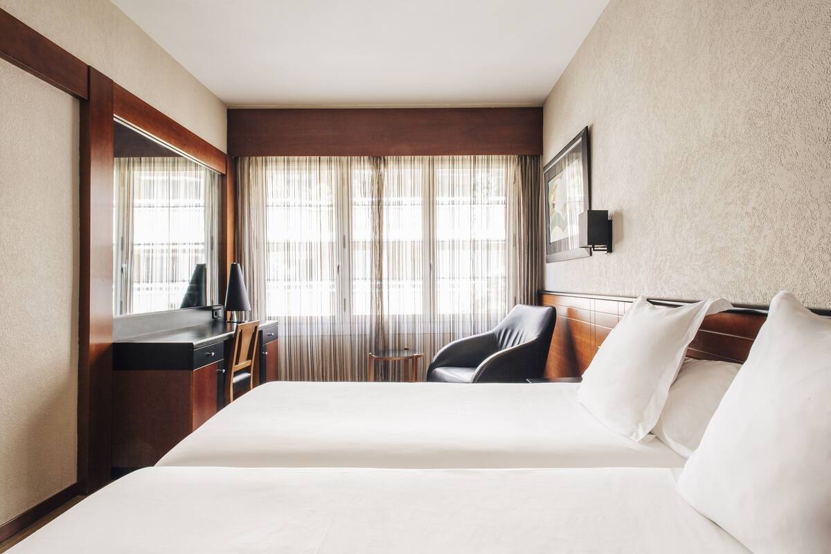 A hotel room with a large bed, a desk, a chair, and a small table.