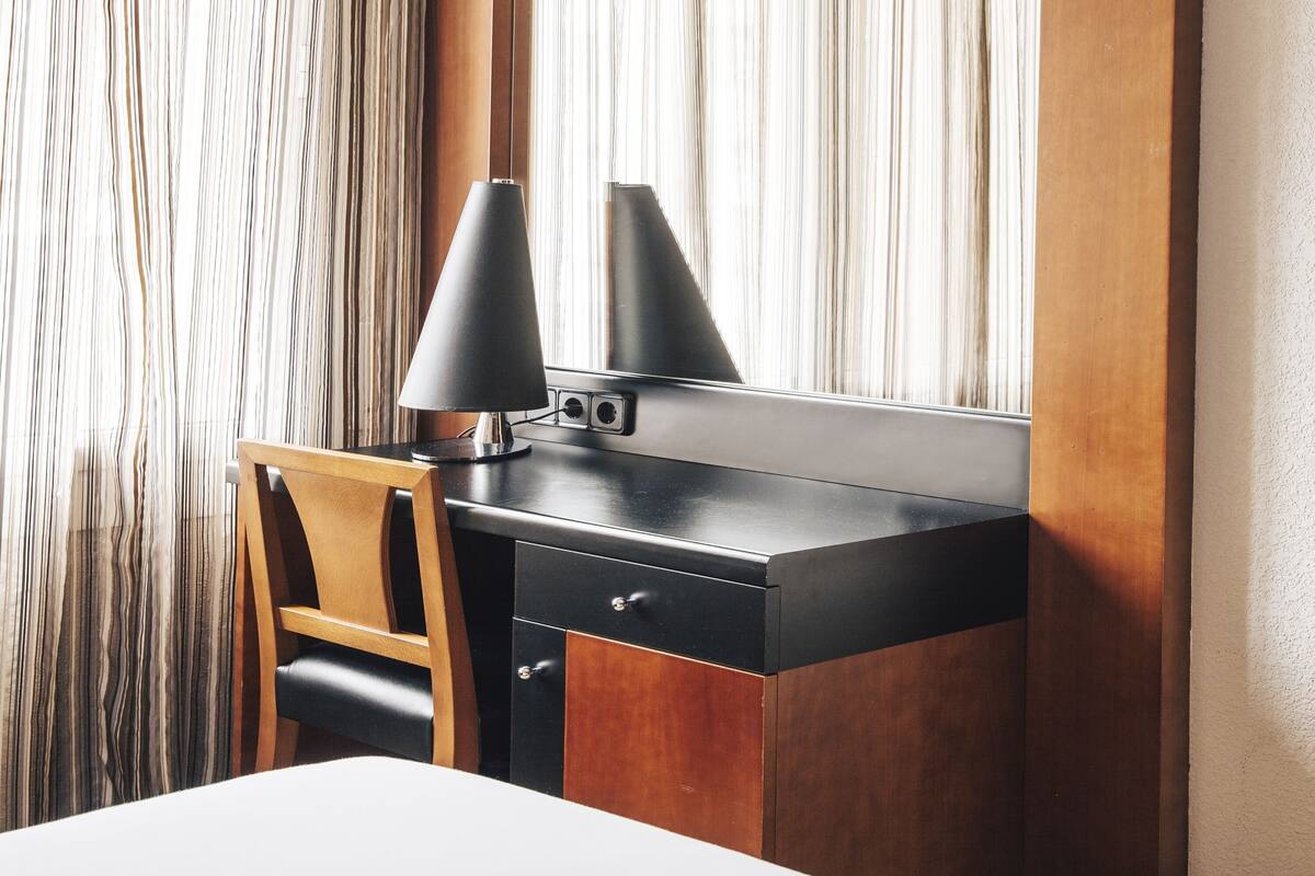 A modern hotel room with a wooden desk, a black lamp, and a mirror.