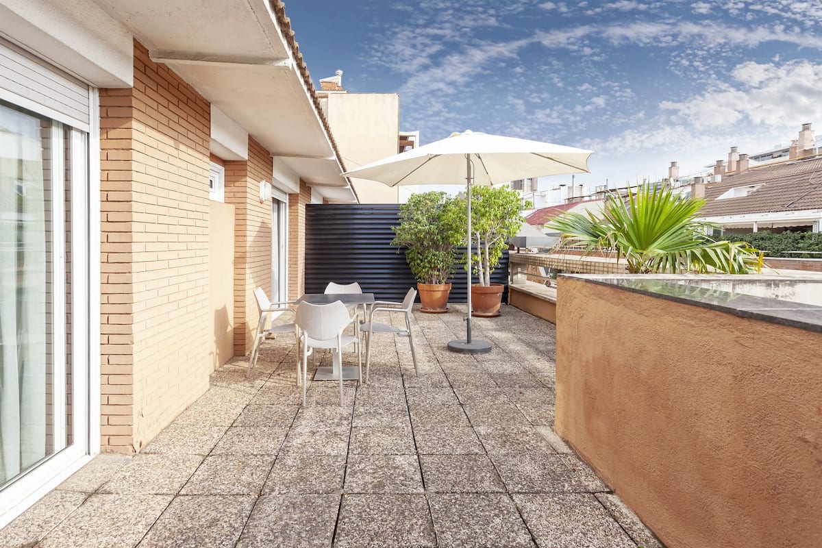 A small outdoor patio with a table and chairs, a potted plant, and a large umbrella.
