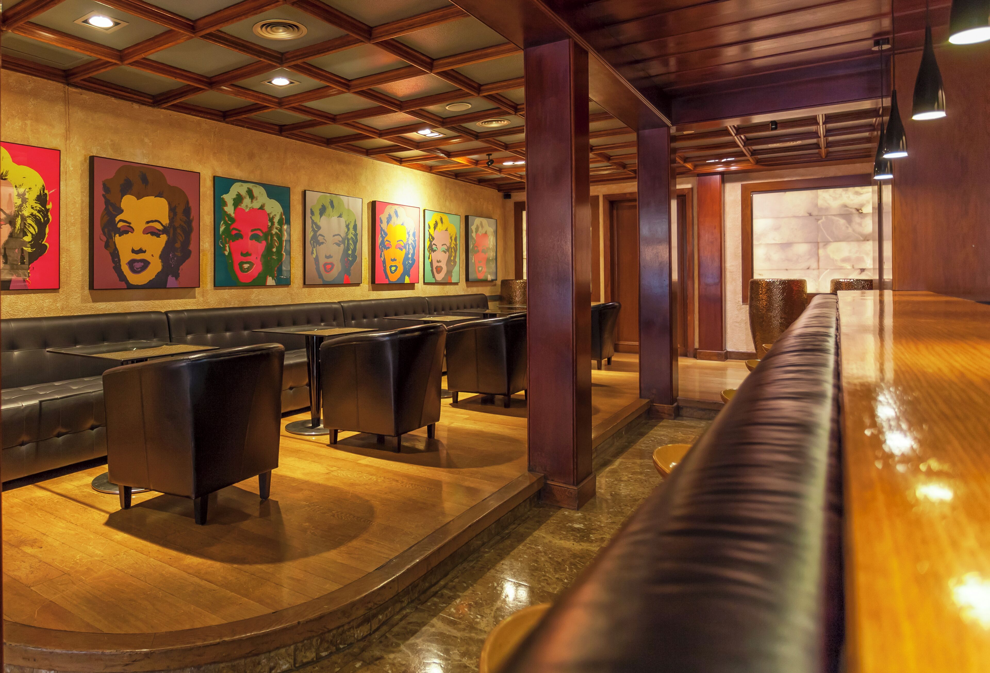 Un restaurante con una barra alargada, cabinas de cuero negro y arte colorido en la pared.
