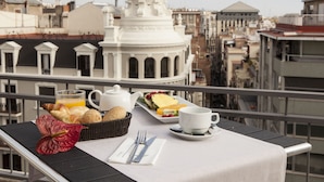 A balcony table with breakfast items, a white teapot, a cup, and a basket of bread.