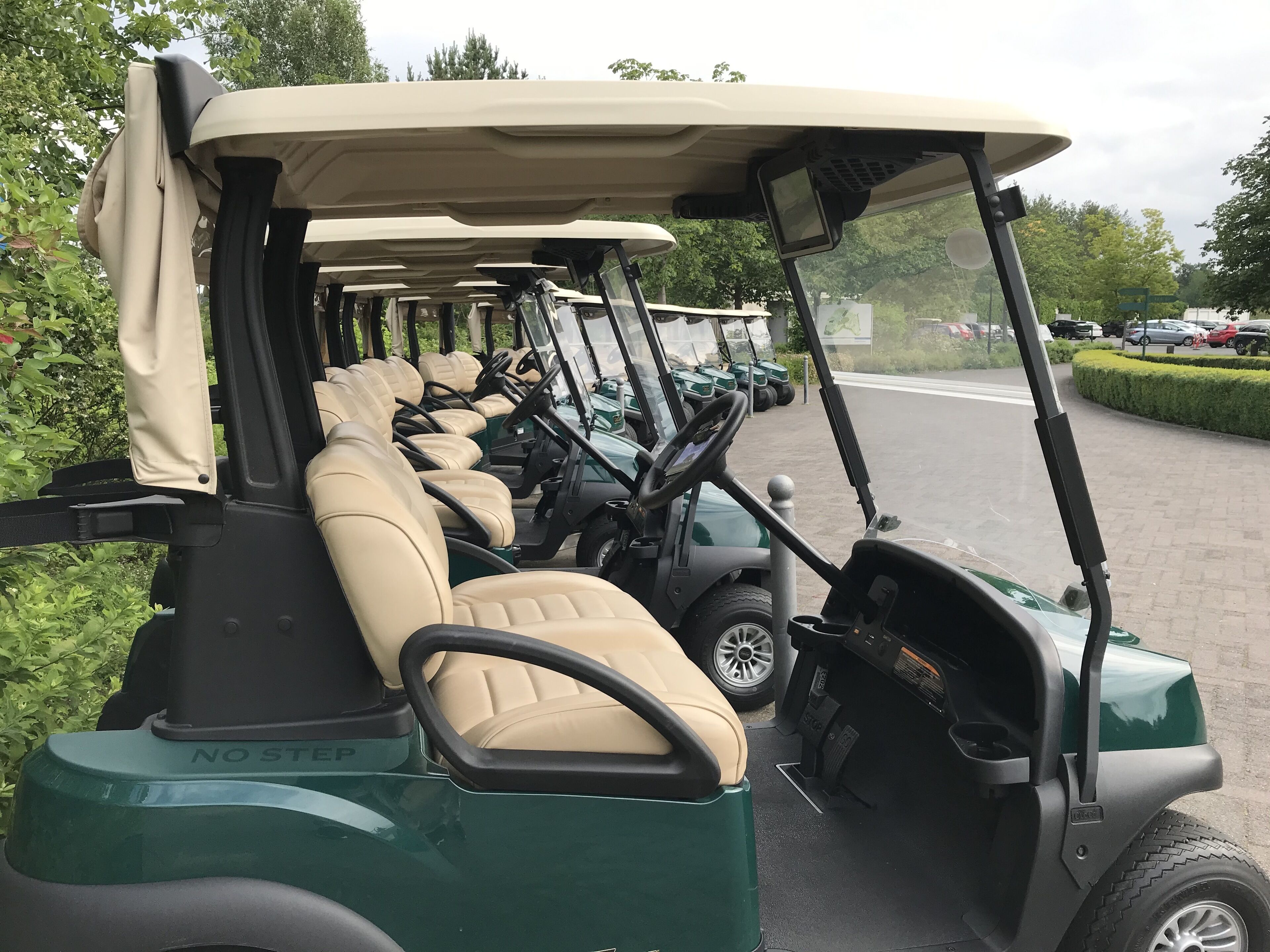 A row of golf carts with beige seats and a "NO STEP" label, parked in a line.