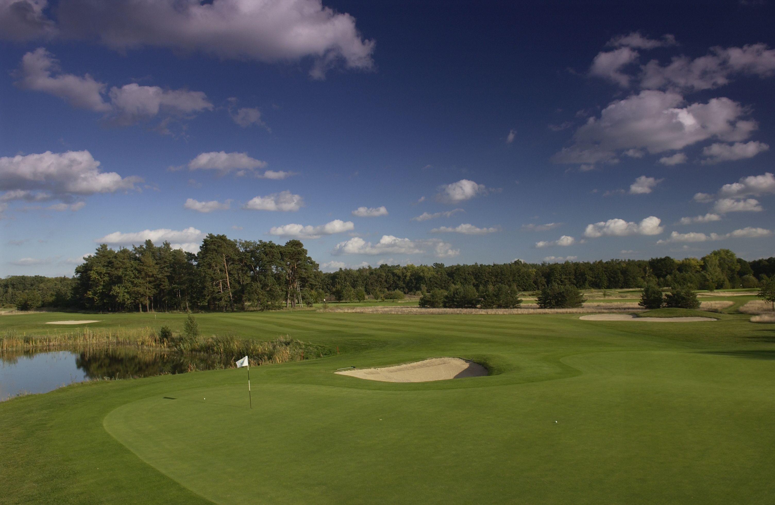 A golf course with a water hazard, sand bunkers, and a flagstick.