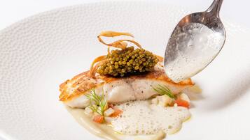 A white plate with a piece of fish topped with caviar, garnished with dill and a sauce.
