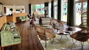 A spacious lobby with a wooden ceiling, green upholstered sofas, wicker chairs, and a large window with curtains. - GolfResort Semlin (Rathenow)