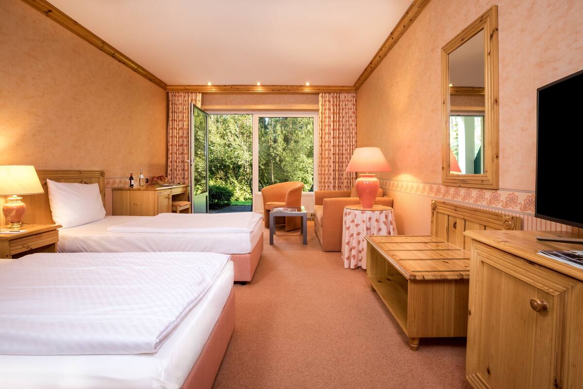 A hotel room with two beds, a desk, a chair, a TV, and a view of the outdoors.