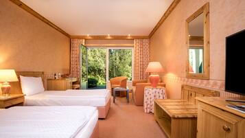 A hotel room with two beds, a desk, a chair, a TV, and a view of the outdoors.