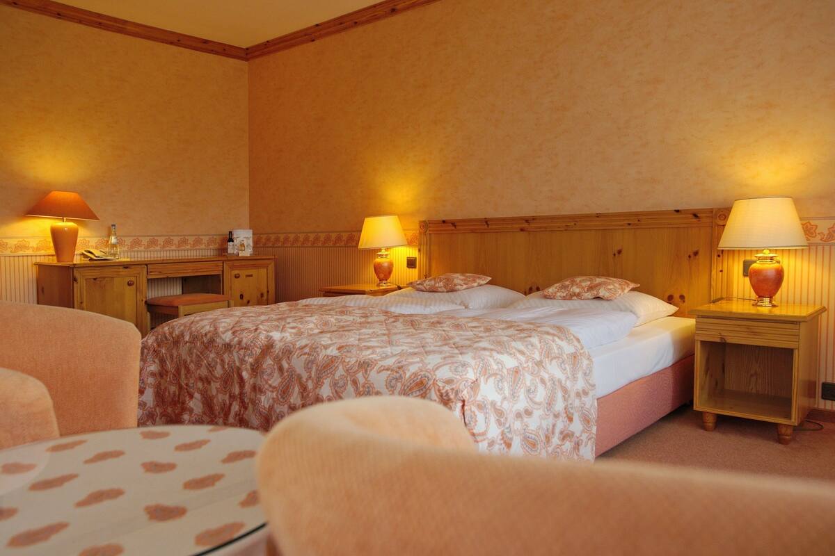 A hotel room with a large bed, two bedside tables with lamps, a small desk, and a chair.