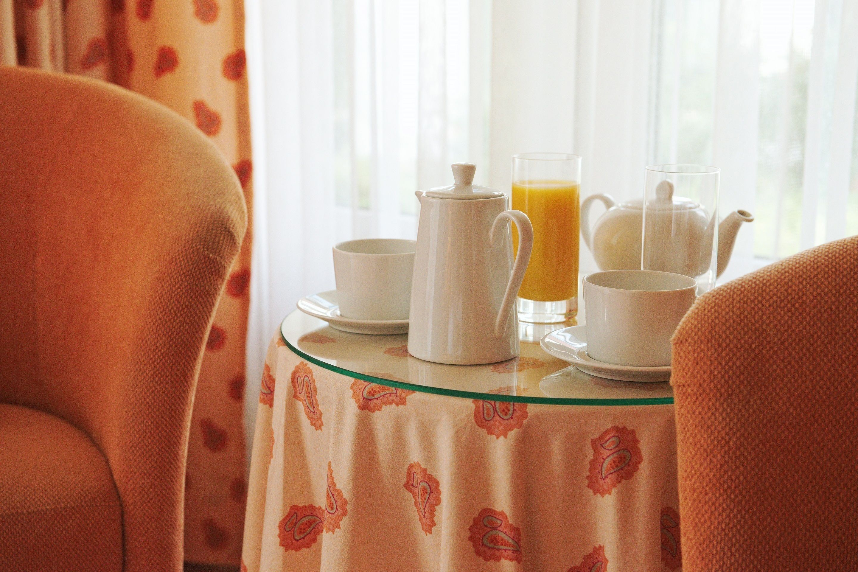 A breakfast table with a pitcher, cups, and a glass of orange juice.