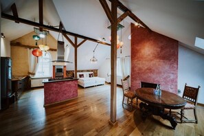 Un loft spacieux avec des poutres apparentes, un îlot central doté de sièges et un coin repas avec une table ronde.