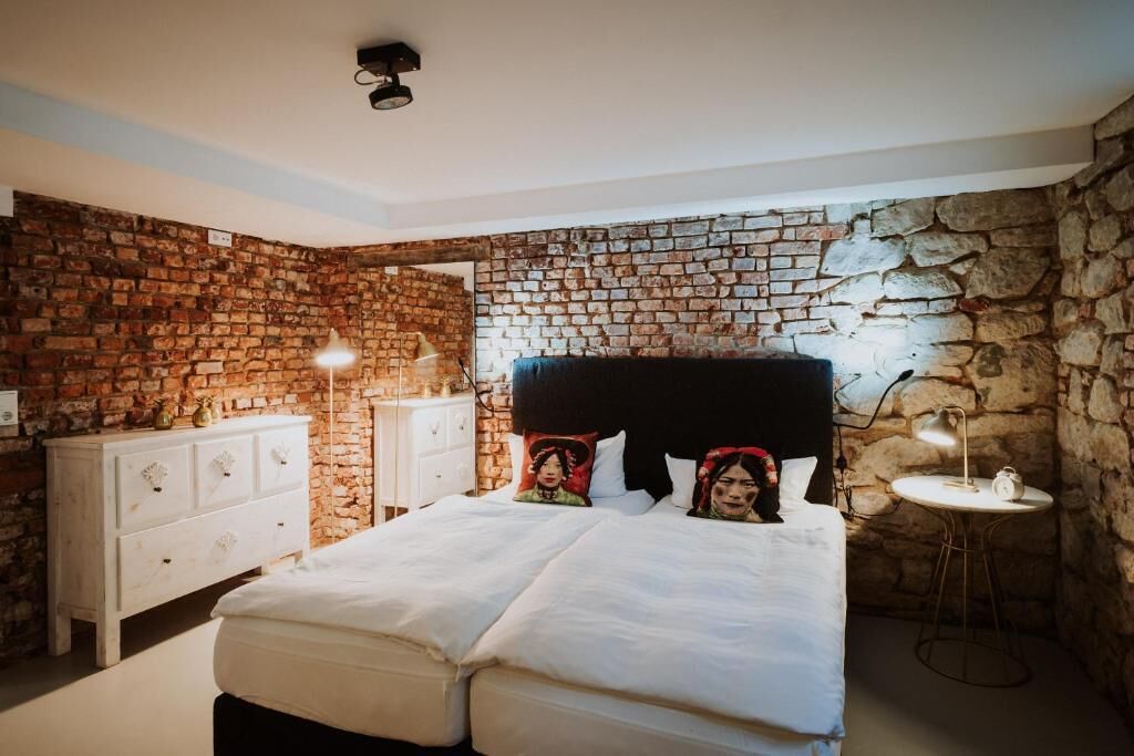 Une chambre avec un mur en briques, un lit avec une literie blanche, une commode blanche et une table de chevet avec une lampe.