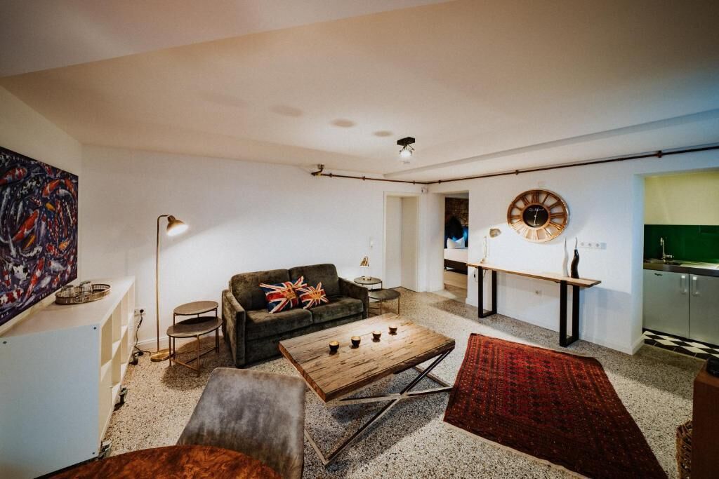 Ein Wohnzimmer mit Sofa, Couchtisch und einem roten Teppich. An der Wand hängt eine Uhr und ein Gemälde.