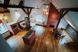 Une pièce mansardée avec un plancher en bois, une table à manger avec des chaises, une cheminée et des lanternes suspendues.