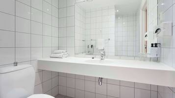 Un baño moderno con baldosas blancas, un espejo grande, un lavabo y un inodoro.