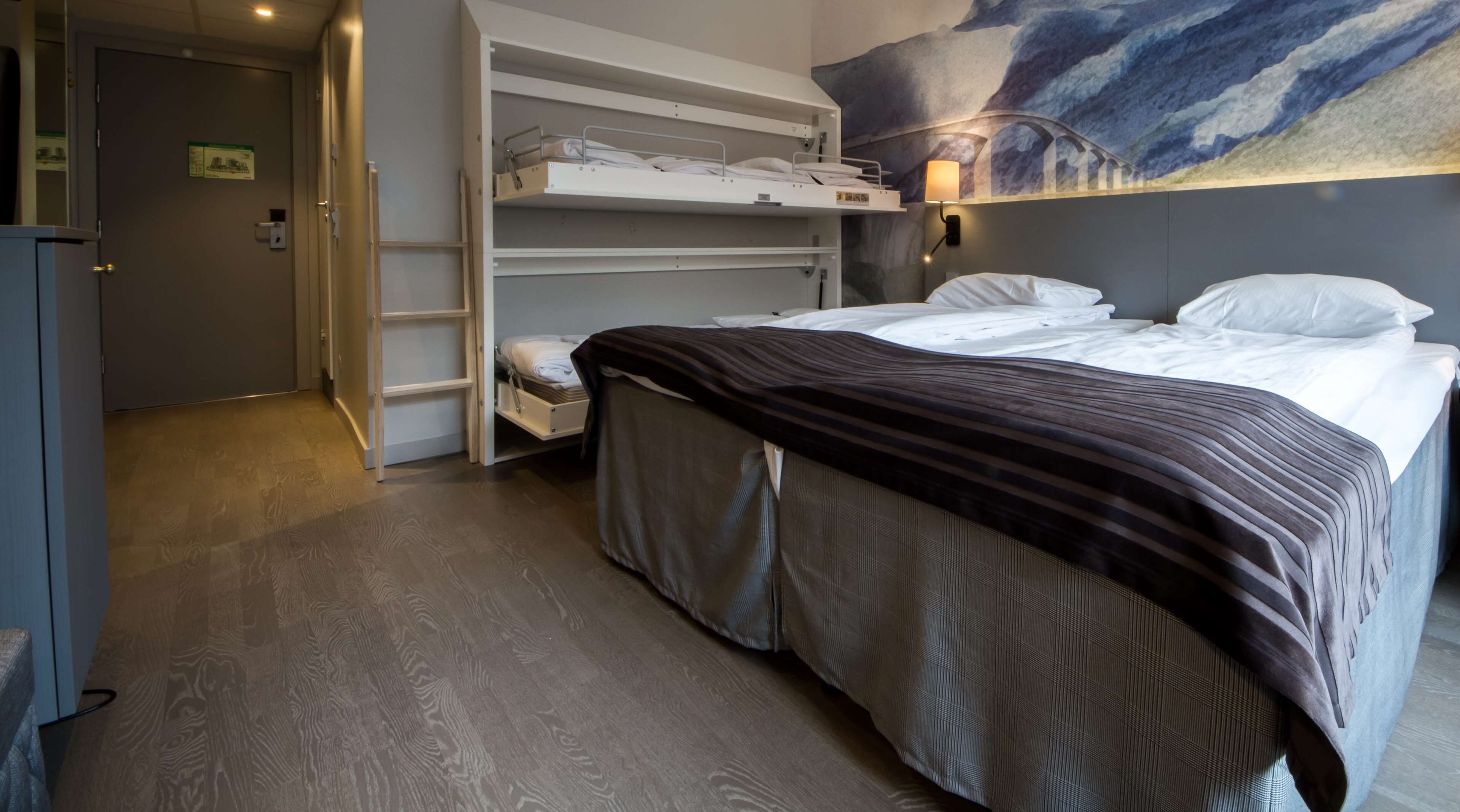 A hotel room with a bed, a wardrobe, a shelf unit, and a painting on the wall.