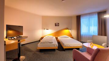 A hotel room with two single beds, a TV, a desk with a chair, and a small table.