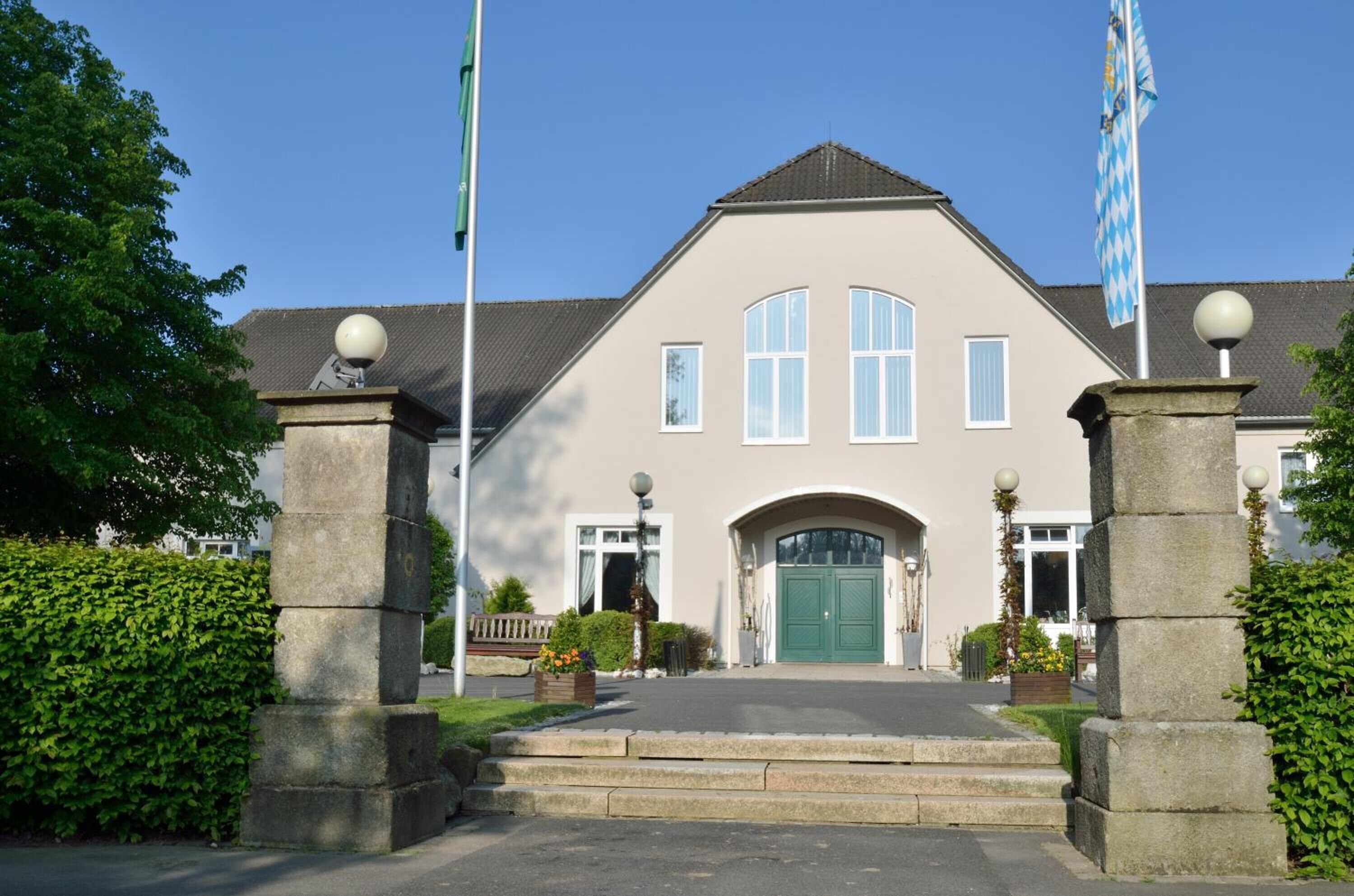 A building with a symmetrical facade, a central entrance with a green door, and two flags on flagpoles.