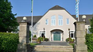 A building with a symmetrical facade, a central entrance with a green door, and two flags on flagpoles.