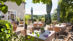 An outdoor patio area with tables and chairs, umbrellas, and potted plants. - Golfhotel Fahrenbach (Trostau)
