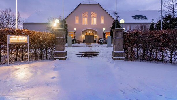A hotel entrance with a snow-covered path leading to a building with a large arched doorway and multiple windows. - Golfhotel Fahrenbach (Trostau)