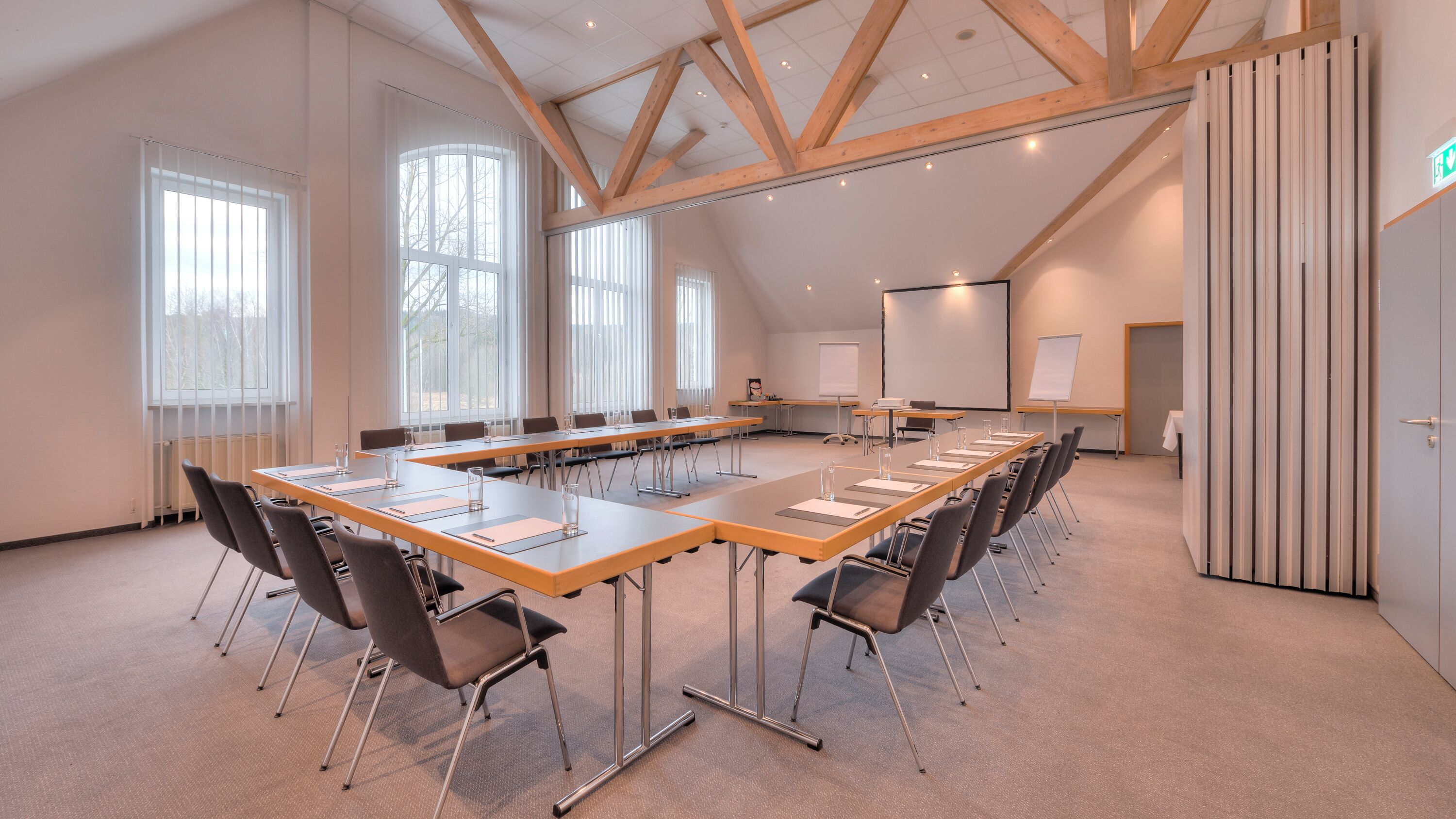 A conference room with a long table, chairs, a whiteboard, and a projector screen.