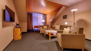 Une chambre d’hôtel confortable avec un plafond en bois, un téléviseur à écran plat, un canapé, une table et une lampe.