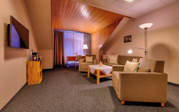 A cozy hotel room with a wooden ceiling, a flat-screen TV, a sofa, a table, and a lamp. - Golfhotel Fahrenbach (Trostau)