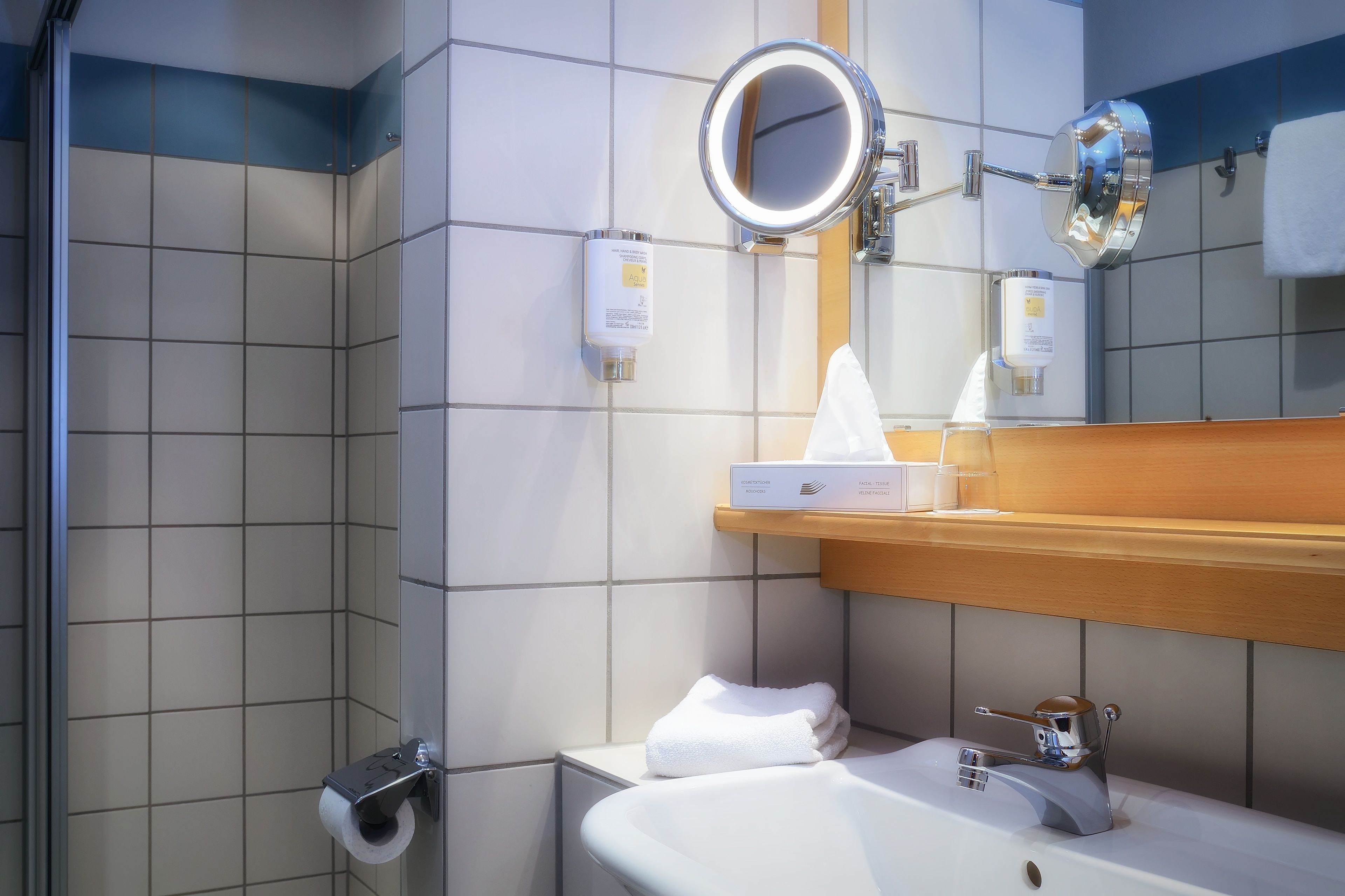 A bathroom with a sink, mirror, towel dispenser, and toilet paper holder.