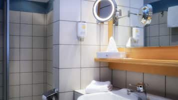 A bathroom with a sink, mirror, towel dispenser, and toilet paper holder.