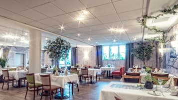 Un restaurante con varias mesas y sillas, pisos de madera y amplios ventanales que dejan entrar luz natural.