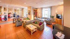 A spacious hotel lobby with multiple seating areas, a television, and a visible clothing store. - Golfhotel Fahrenbach (Trostau)