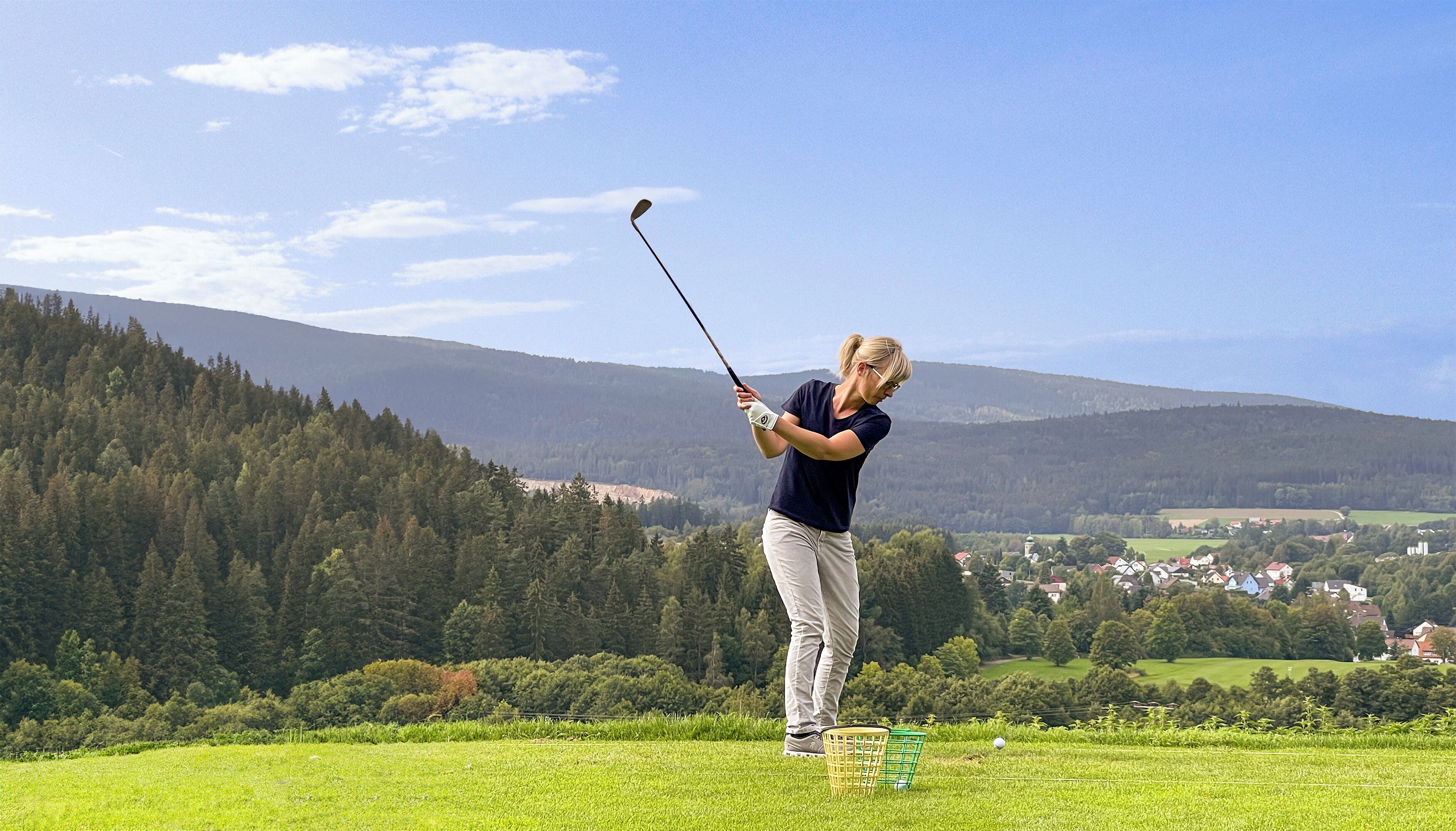Una persona jugando al golf en un campo verde con imponentes montañas al fondo.