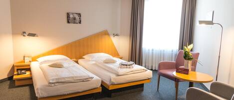 Ein Hotelzimmer mit zwei Betten, einem kleinen Tisch, einem Stuhl und einer Lampe.