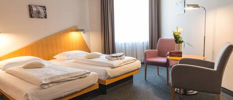 Habitación de hotel con dos camas, un escritorio, una silla, una lámpara y una ventana con cortinas.