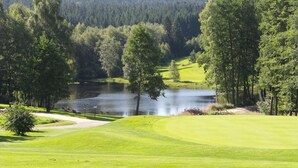 A golf course with a pond, surrounded by trees and a forest in the background. - Golfhotel Fahrenbach (Trostau)