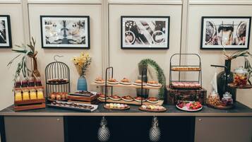 A buffet setup with various food items and drinks, framed artwork on the wall, and a decorative plant.