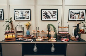 Ein reichhaltiges Buffet mit verschiedenen Speisen und Getränken, Kunstwerke an der Wand und eine Zierpflanze.