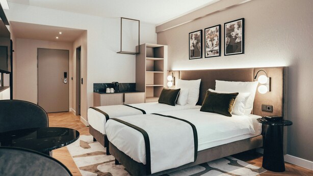 Ein modernes Hotelzimmer mit Doppelbett, Nachttischen, einem Schreibtisch und einem Stuhl.