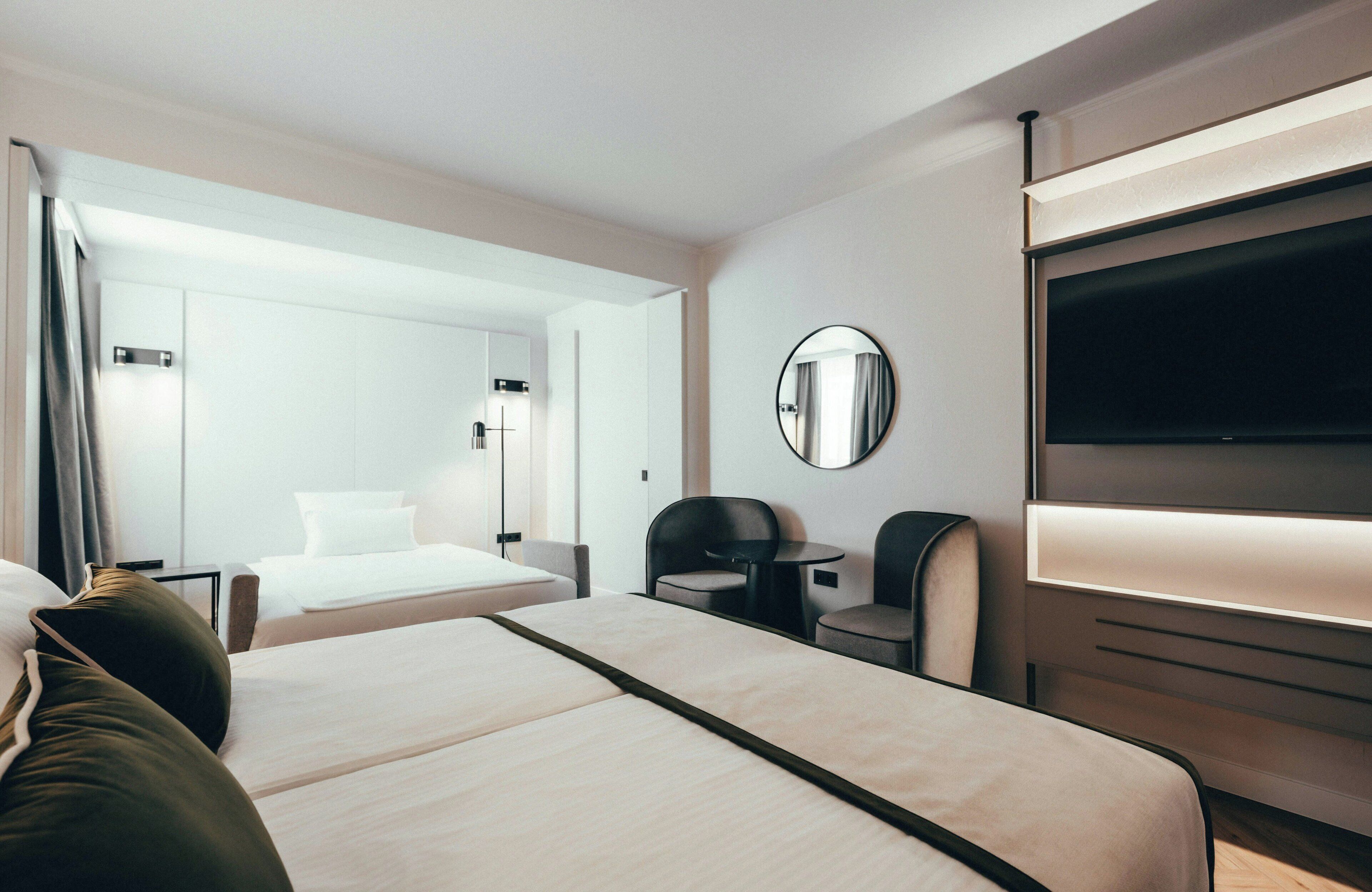 Ein modernes Hotelzimmer mit Bett, Schreibtisch, Stuhl, Fernseher und Spiegel.