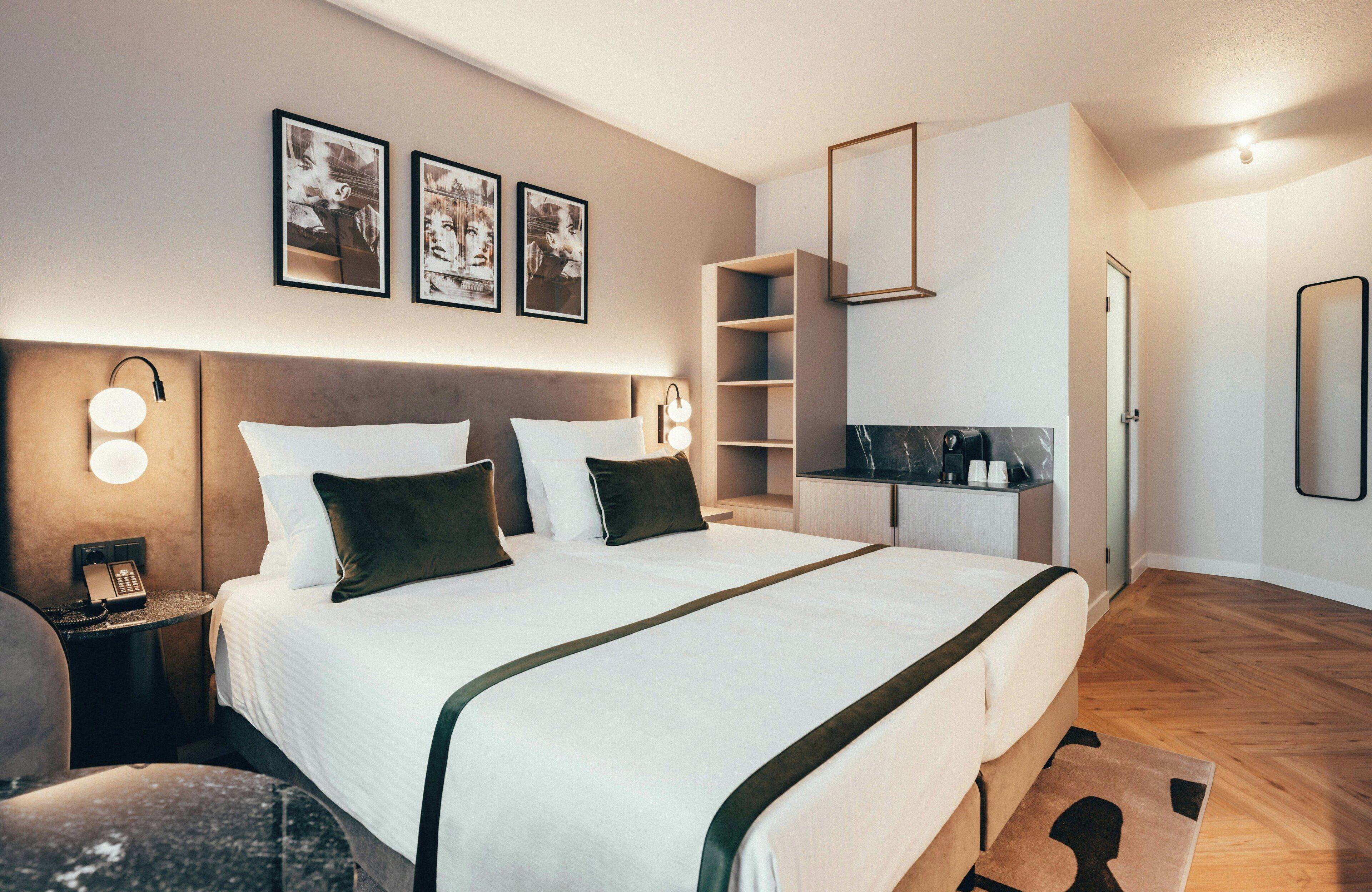 Ein modernes Hotelzimmer mit einem großen Bett, Nachttischlampen, einem Schreibtisch mit Telefon und einem Spiegel an der Wand.