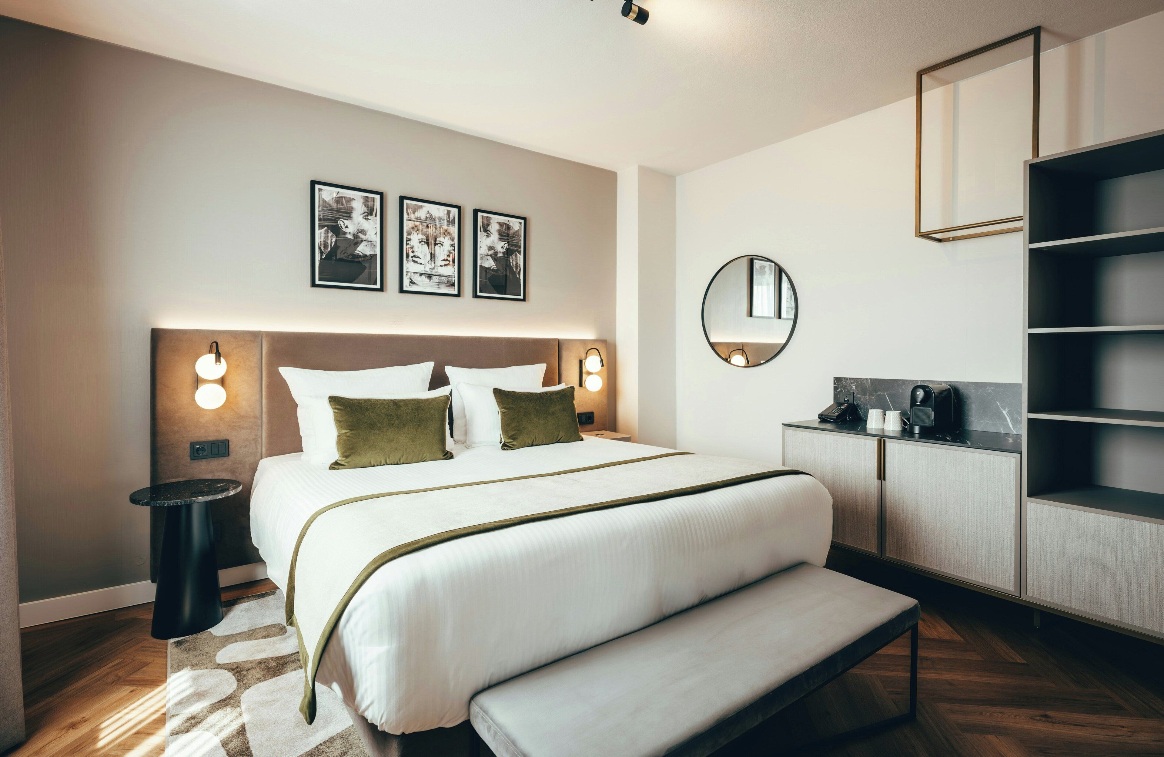 Ein modernes Hotelzimmer mit einem großen Bett, Nachttischen, einem runden Spiegel und einem eingebauten Kleiderschrank.