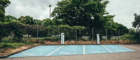 Een parkeerplaats met blauwe parkeerplaatsen en een hek met bomen op de achtergrond.