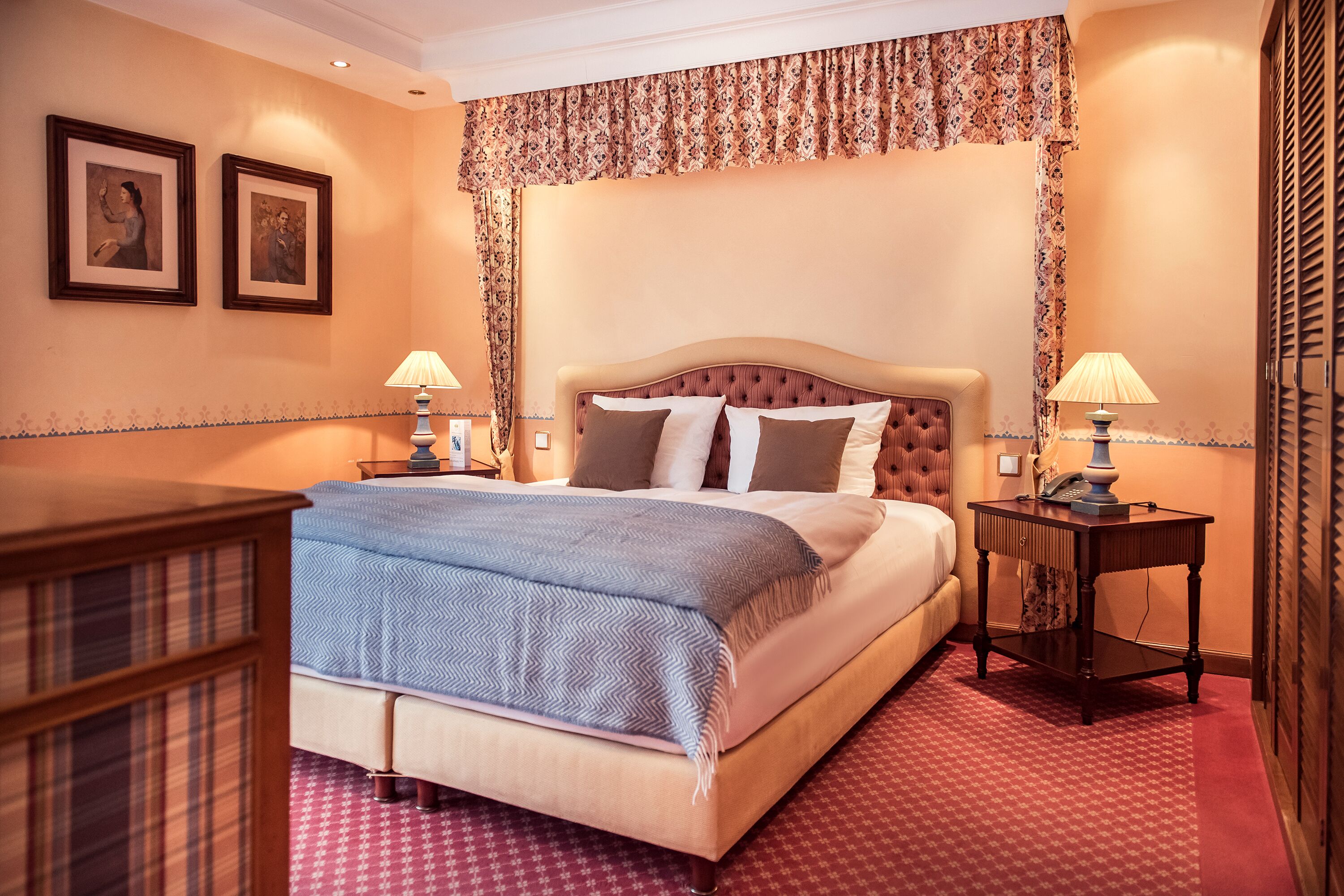 Una habitación de hotel con una cama grande, dos mesitas de noche, un aparador y un armario.