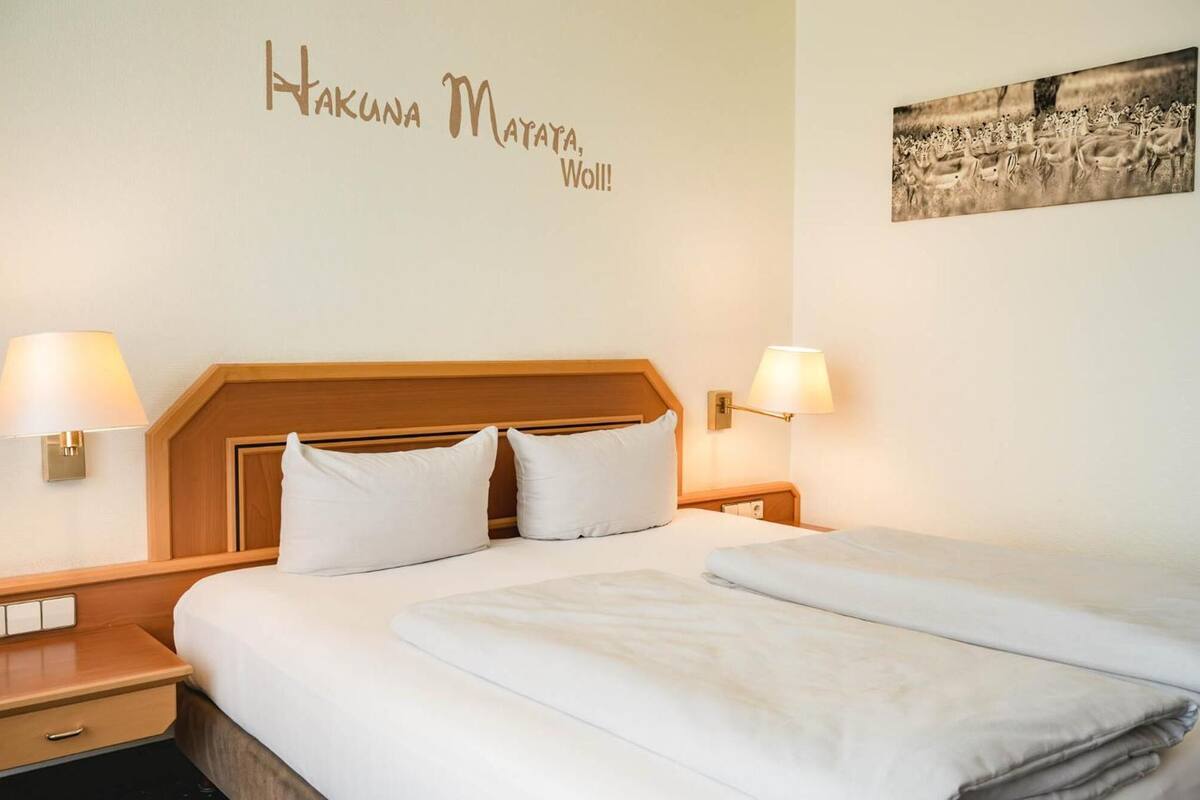A hotel room with a double bed, two bedside tables, wall-mounted lamps, and a framed picture.