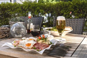Una mesa de madera con una comida que incluye huevos, carnes y verduras, acompañada de una cerveza y una botella de vino.