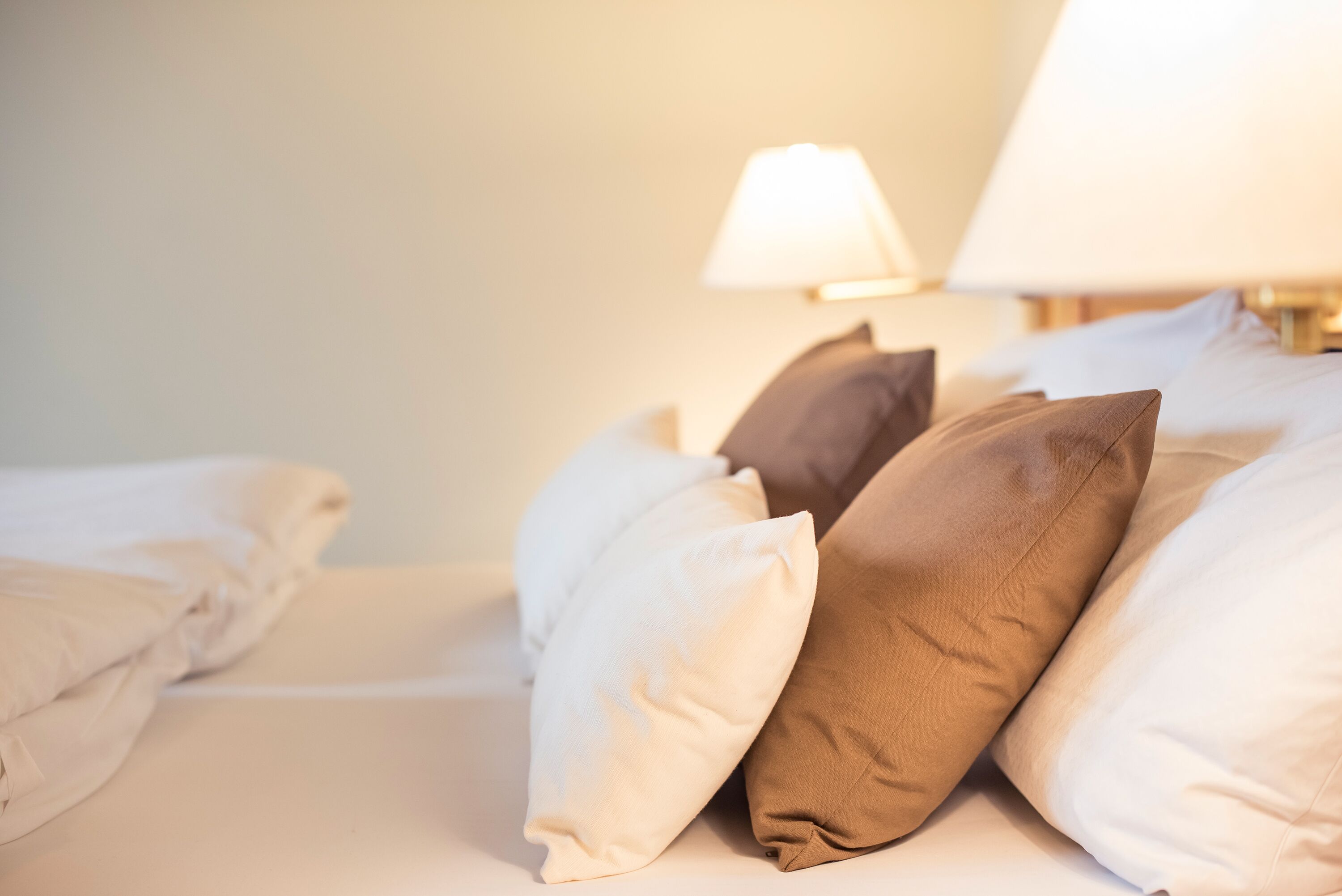 Un lit bien fait, agrémenté de plusieurs oreillers et d’une lampe de chevet.