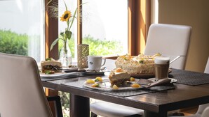 Una mesa de comedor con un pastel, una taza y una taza de café, frente a una ventana con vistas a zonas verdes.
