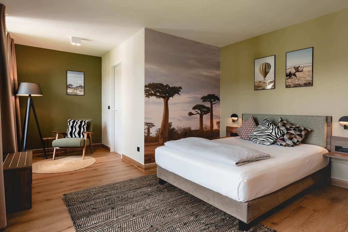 A bedroom with a large bed, a chair, a lamp, and a wall mural.